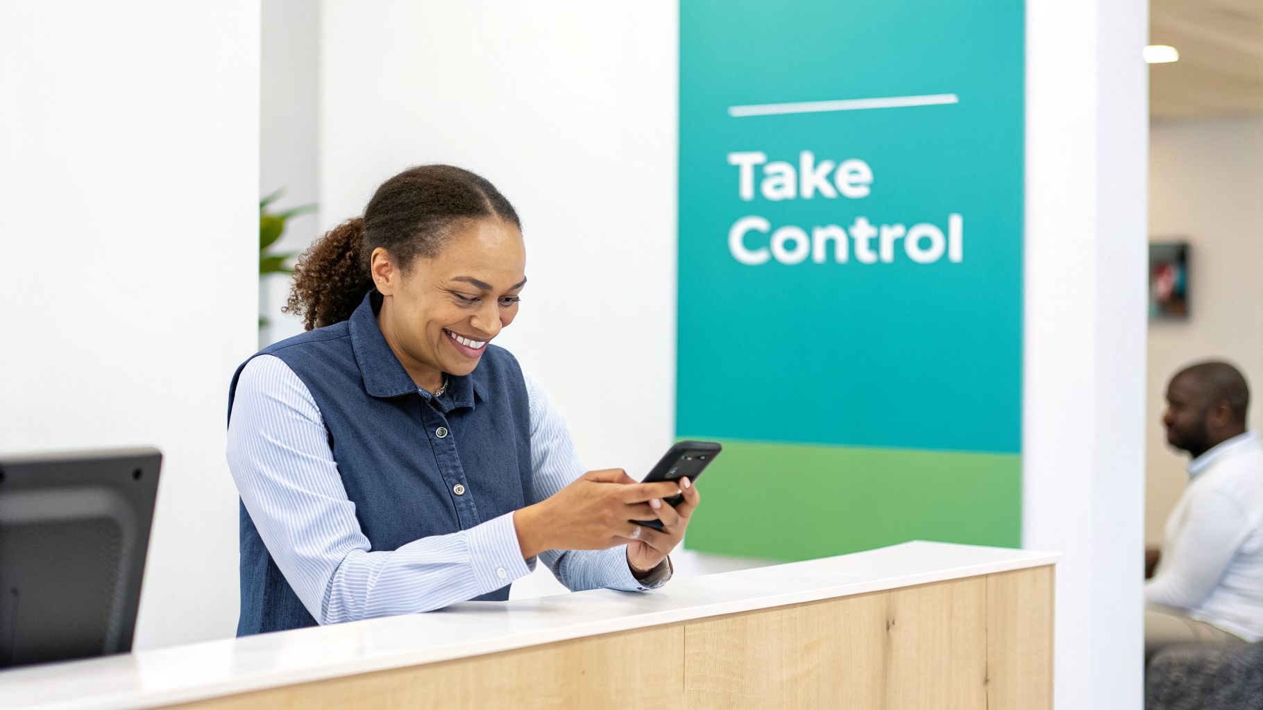 A smiling woman in a denim vest and striped shirt uses her smartphone at a reception desk.